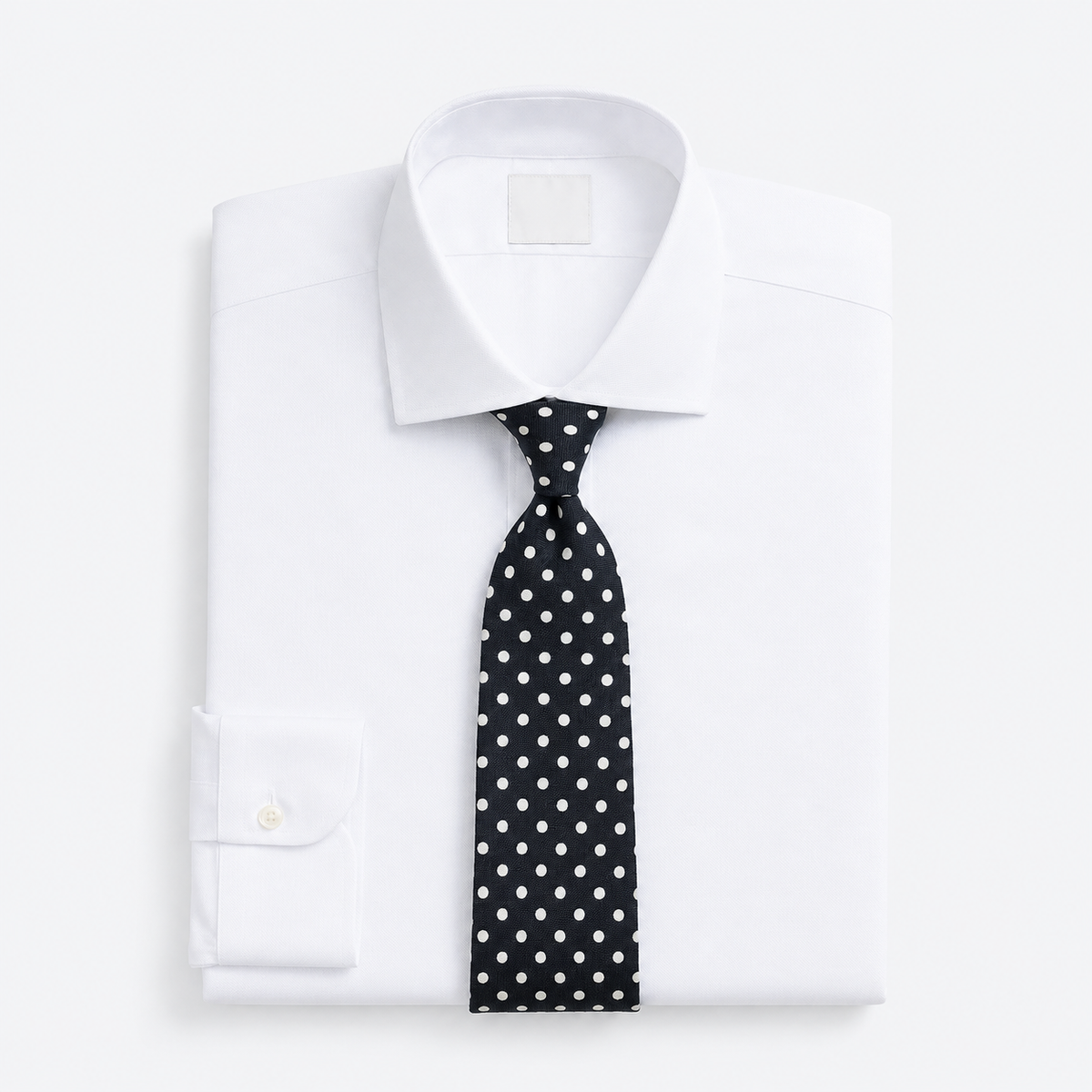 Folded white dress shirt with a spread collar and a black tie with white polka dots.